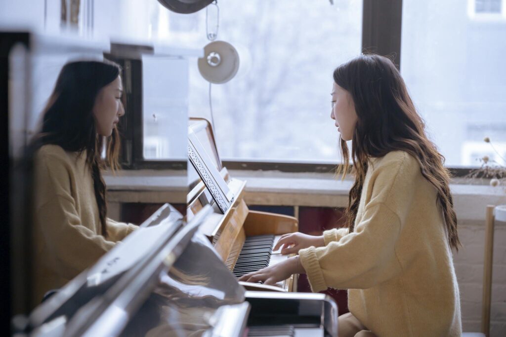 Side view of young ethnic female pianist playing piano while watching music score during rehearsal